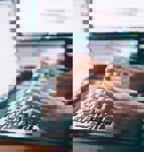 Två händer i fokus på någon som skriver på en laptop.