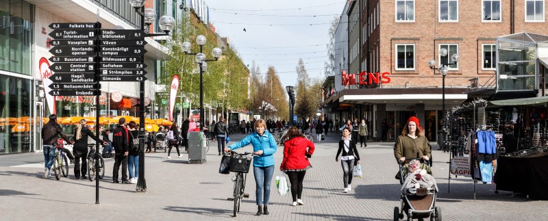 Bild på en gågata i Umeå centrum med människor som går, leder en cykel coh går med barnvagn.