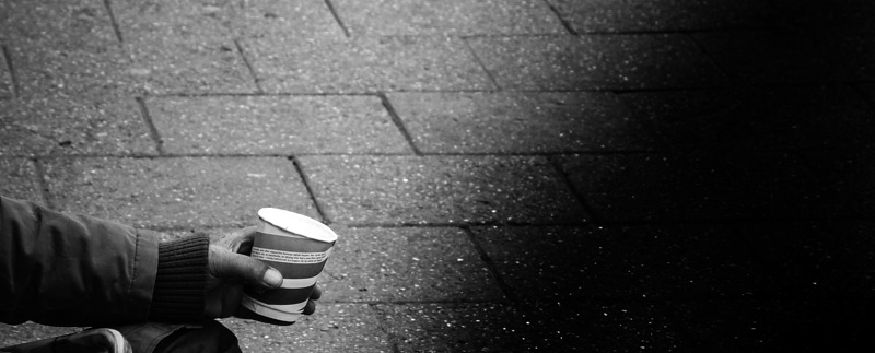 Person som sitter på gatan med framsträckt pappersmugg.