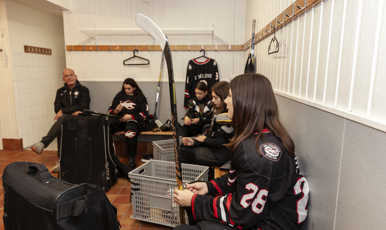Tonårstjejer med sin tränare i ett omklädningsrum under hockeyträning