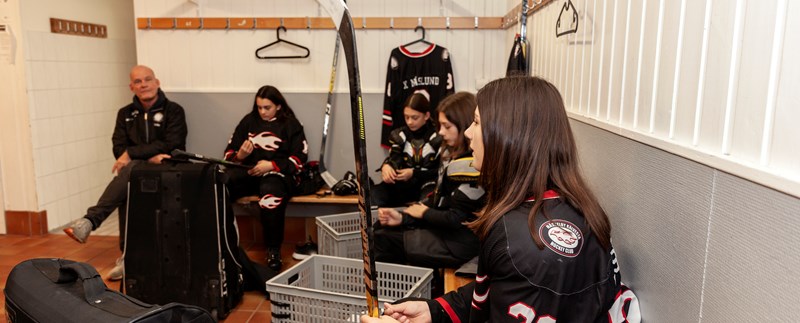 Tonårstjejer med sin tränare i ett omklädningsrum under hockeyträning