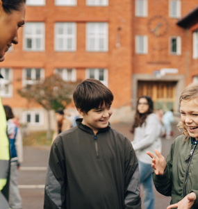 En rastvakt pratar med tre elever på en skolgård.