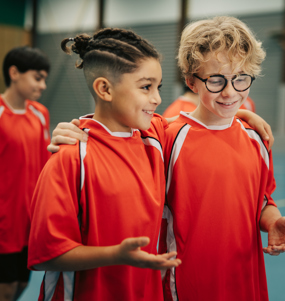 Två killar i träningskläder i en sporthall är glada, pratar och håller armen om varandra.