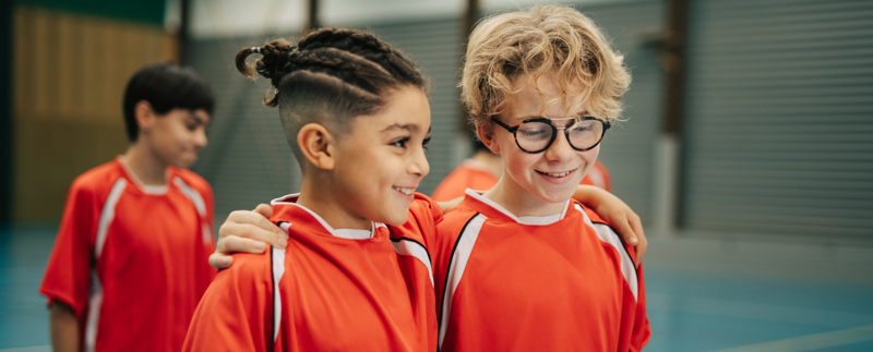 Två killar i träningskläder i en sporthall är glada, pratar och håller armen om varandra.