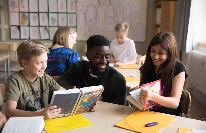 Elever i mellan- eller högstadieåldern tittar i böcker tillsammans med sin lärare. 