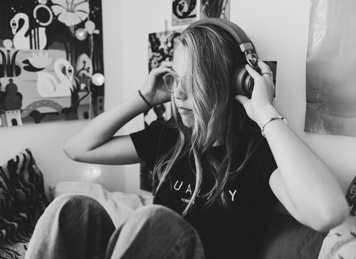 Flicka sitter i sitt tonårsrum och håller sina hörlurar mot öronen