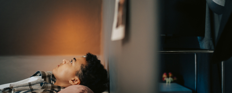 Ung person ligger i en säng och tittar upp i taket.