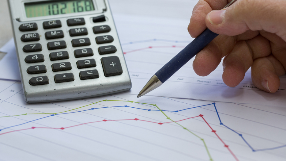 Miniräknare och en hand som håller i en penna för att analysera statistik.