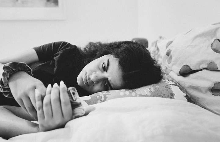 Ung kvinna ligger i en säng och läser meddelande på sin telefon med bekymrat ansiktsuttryck
