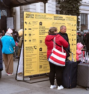 Människor med resväskor bredvid en informationsskylt på ukrainska.