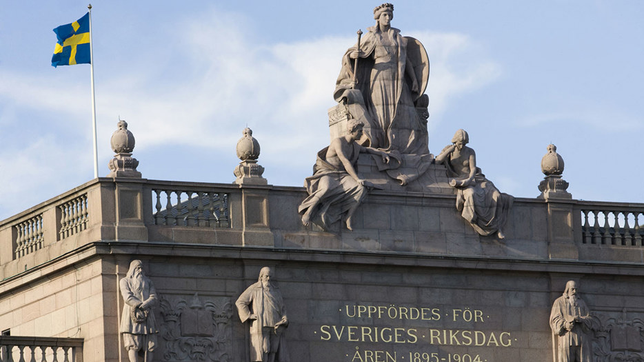 Stenskulpturer och svenska flaggan på riksdagshuset övre del.