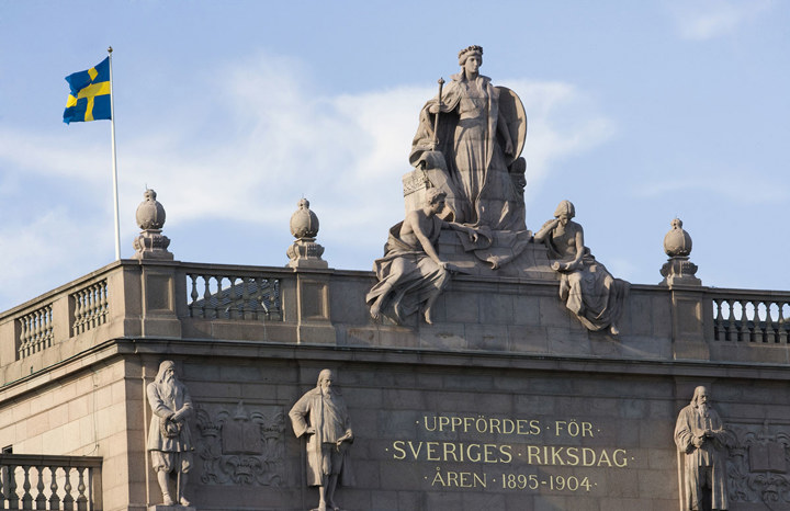 Stenskulpturer och svenska flaggan på riksdagshuset övre del.