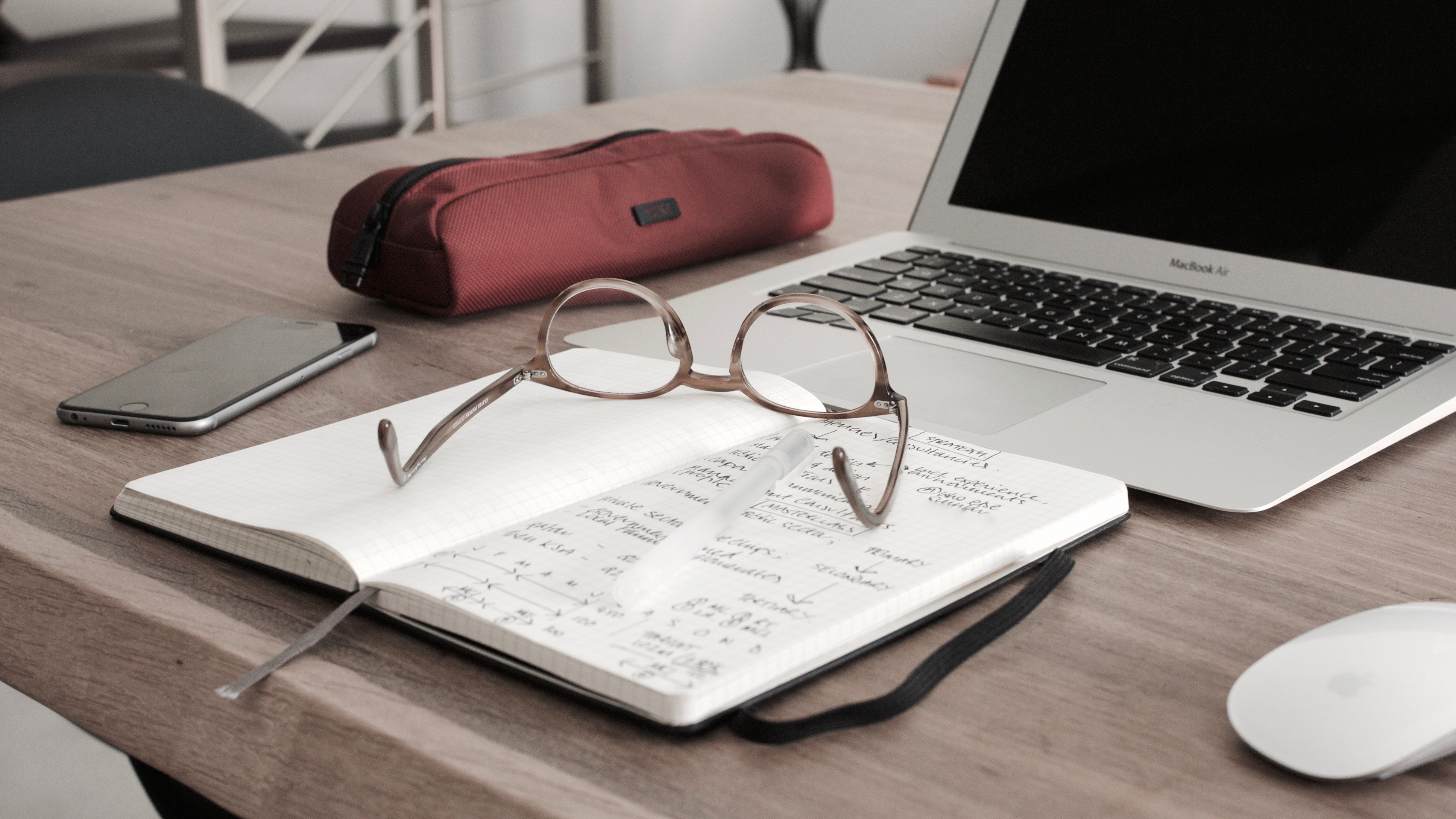 Ett anteckningsblock ligger på ett bord framför en laptop. Ett par glasögon ligger på blocket.