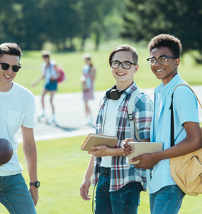 Tre tonårskillar i en park med en boll och varsin ryggsäck
