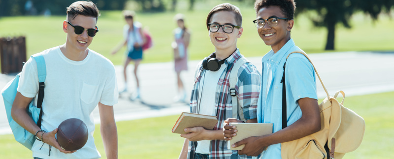 Tre tonårskillar i en park med en boll och varsin ryggsäck