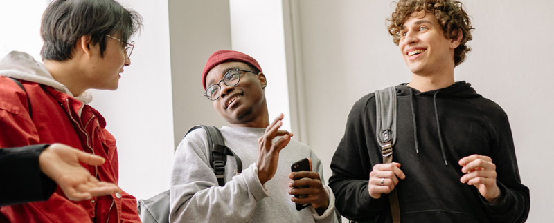 Tre unga killar samtalar med varandra i en ljus inomhusmiljö