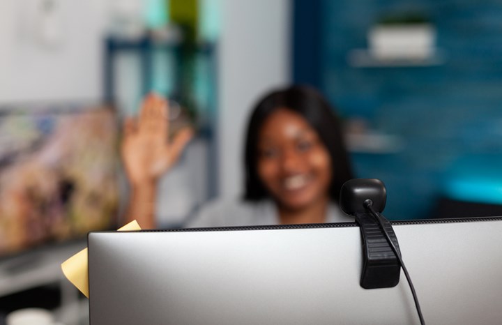 Kvinna räcker upp handen framför en laptop. Skärmen syns inte men har en webbkamera monterad i överkant.