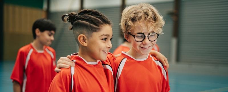 Två glada killar i en idrottshall håller armarna om varandra och pratar.