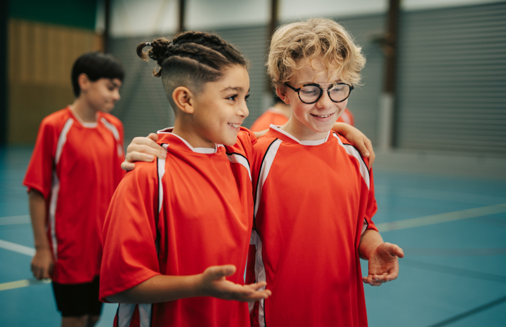 Två glada killar i en idrottshall håller armarna om varandra och pratar.