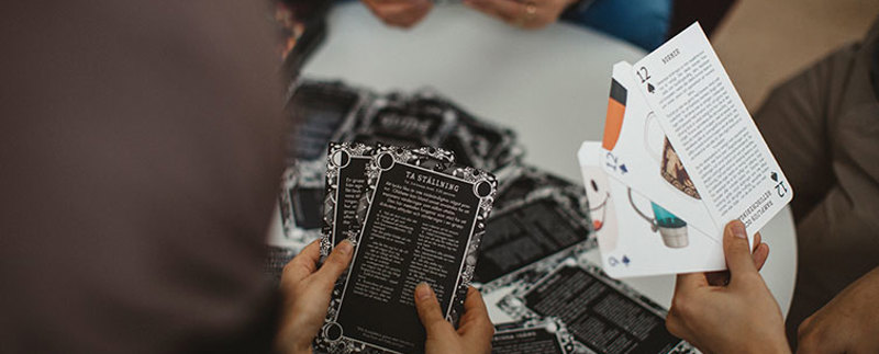 Händer och bakhuvudet syns på tre personer som spelar ett kortspel som handlar om normkritik