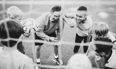 En fotbollstränare och några unga fotbollsspelare står i ring på en plan.