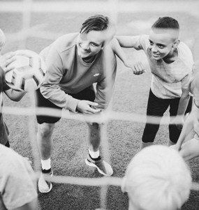 En fotbollstränare och några unga fotbollsspelare står i ring på en plan.