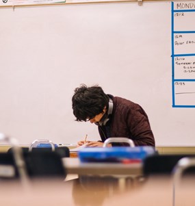 Manlig student böjd över böcker ensam i ett klassrum