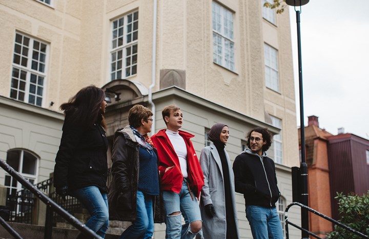 Fem personer som går nerför en trappar utomhus utanför en universitetsbyggnad. De ler och är i samtal med varandra.