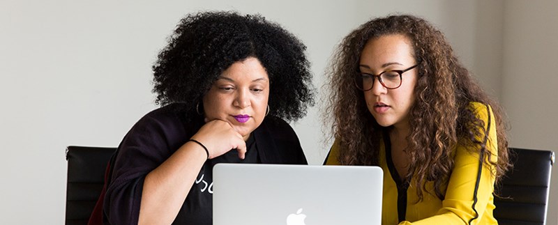 Två kvinnor som tillsammans tittar på skärmen på en laptop