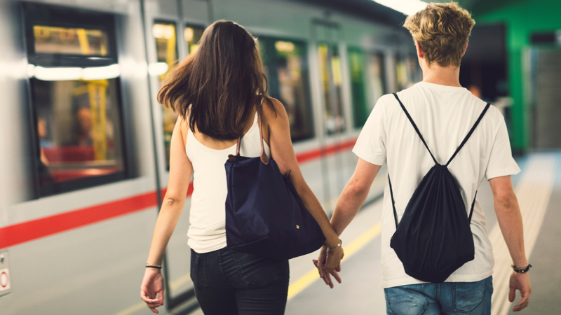 Ett ungt par som håller handen och promenerar längst en tågperrong.