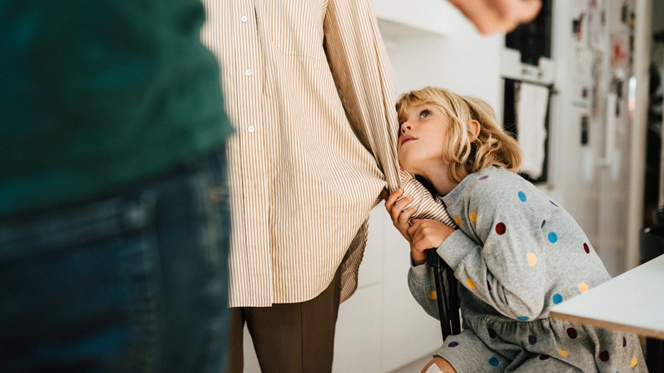 En flicka som hänger i sin mammas skjortärm, tittar oroligt upp på föräldrarna.