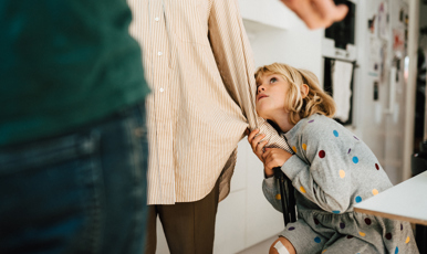 En flicka som hänger i sin mammas skjortärm, tittar oroligt upp på föräldrarna.