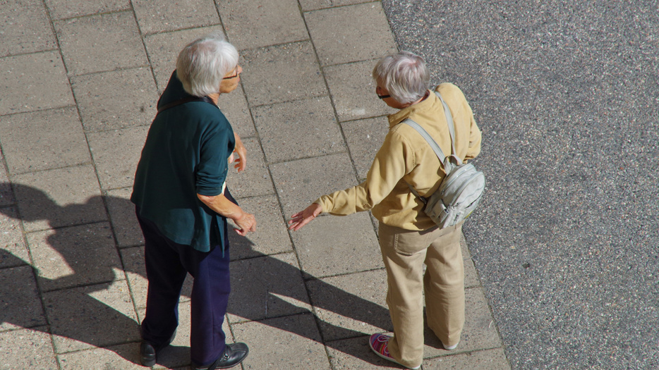 Två äldre personer samtalar på en gata.