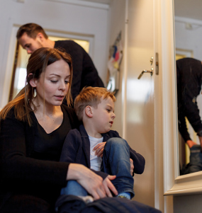 En familj med två mindre barn klär på sig i en hall.